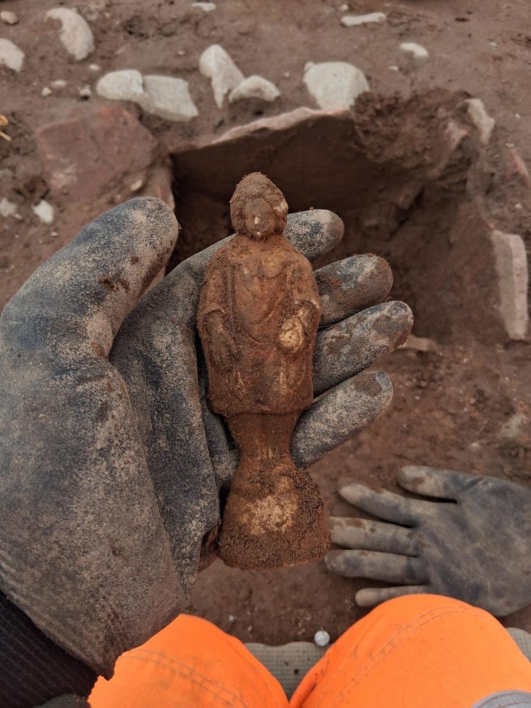 Archaeologist working in a trench holding up a clay statuette.